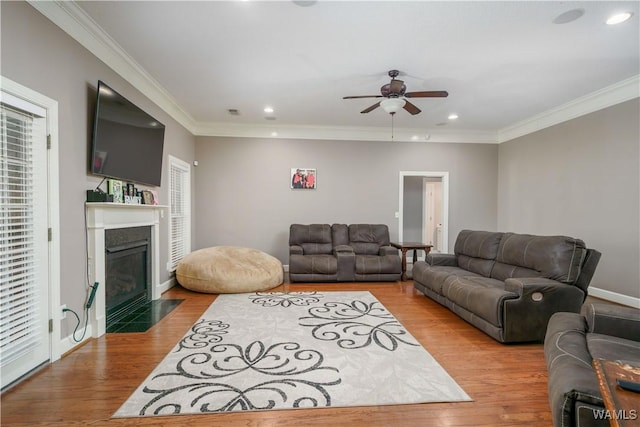 living room with recessed lighting, light wood-style flooring, ornamental molding, a fireplace with flush hearth, and ceiling fan