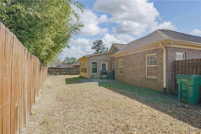 back of property with a patio area, a fenced backyard, roof with shingles, and brick siding