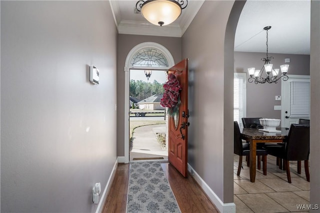 doorway featuring arched walkways, crown molding, baseboards, and wood finished floors