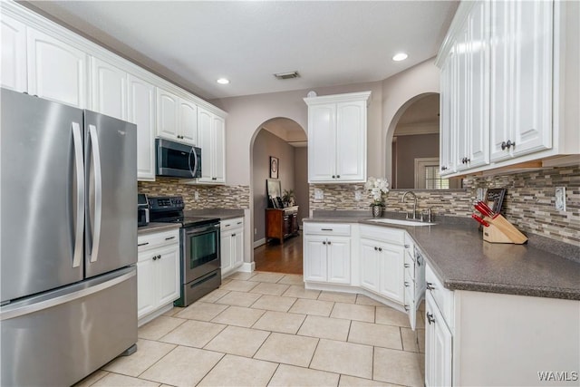 kitchen featuring stainless steel appliances, dark countertops, white cabinetry, and a sink