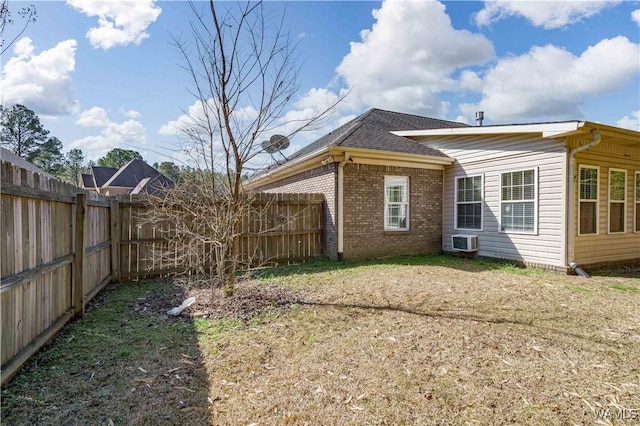 back of property with brick siding, a yard, a shingled roof, a fenced backyard, and a wall mounted air conditioner