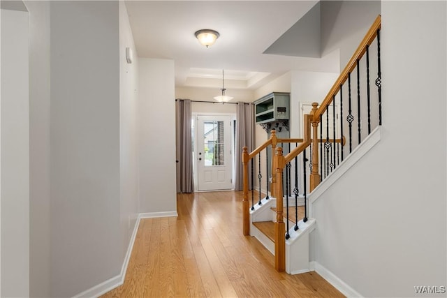 foyer with light wood-type flooring, stairway, baseboards, and a raised ceiling