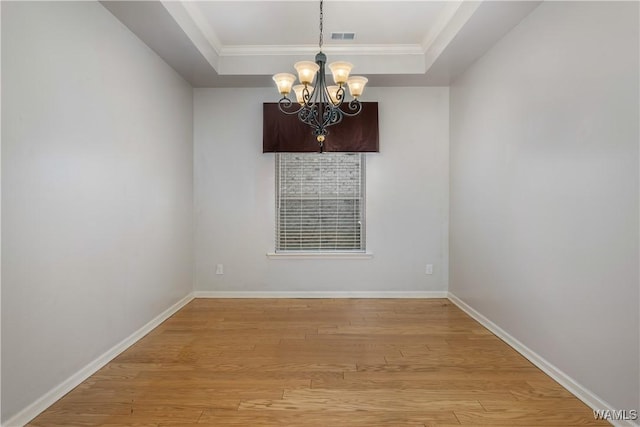 spare room with a notable chandelier, visible vents, baseboards, light wood-style floors, and a raised ceiling