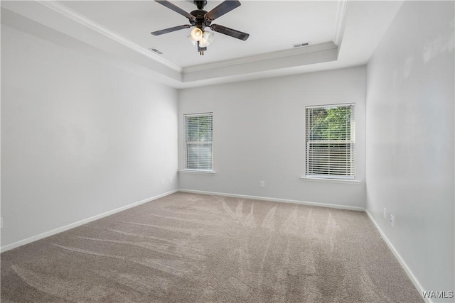 carpeted empty room with baseboards, a tray ceiling, visible vents, and crown molding