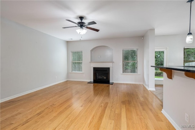 unfurnished living room featuring light wood finished floors, ceiling fan, baseboards, and a glass covered fireplace