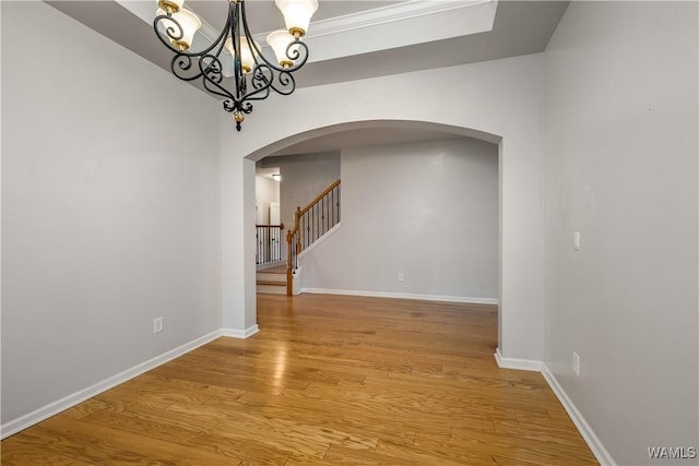 unfurnished room featuring arched walkways, light wood finished floors, stairway, and baseboards