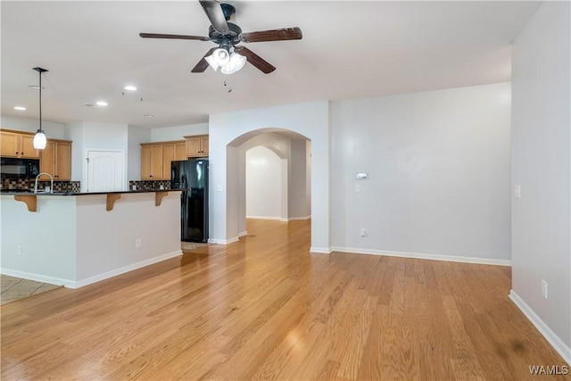 kitchen with arched walkways, a breakfast bar, open floor plan, black appliances, and dark countertops