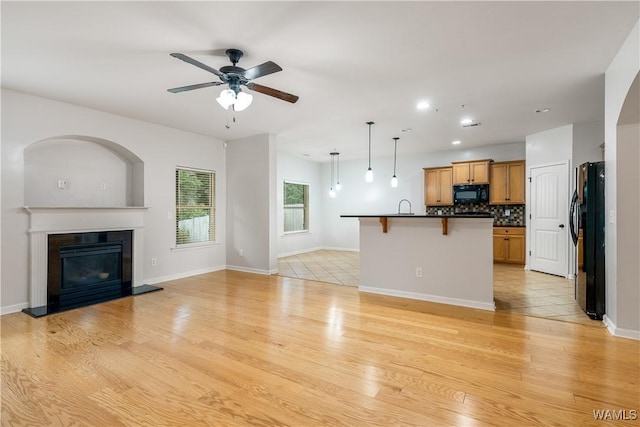 kitchen with a breakfast bar, open floor plan, black appliances, dark countertops, and a glass covered fireplace