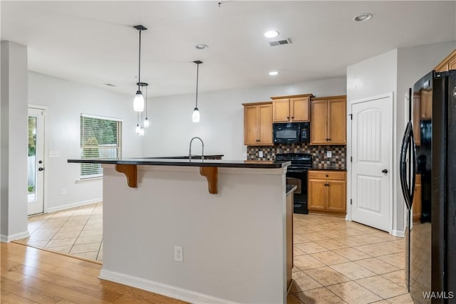 kitchen featuring visible vents, black appliances, tasteful backsplash, dark countertops, and a kitchen bar