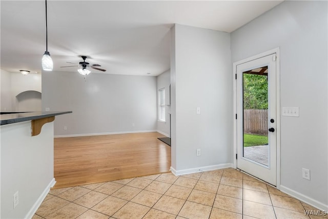 interior space with a ceiling fan, baseboards, and light tile patterned floors