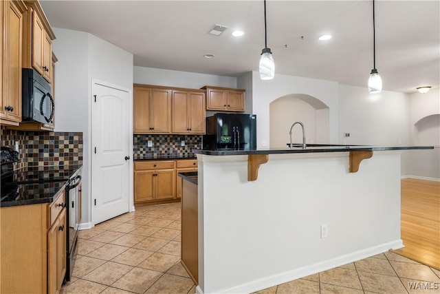 kitchen with dark countertops, black appliances, light tile patterned floors, and a breakfast bar area