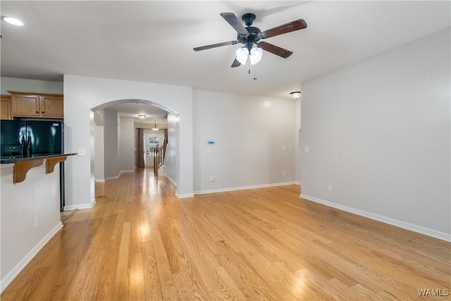 unfurnished room featuring arched walkways, a ceiling fan, baseboards, stairway, and light wood-type flooring