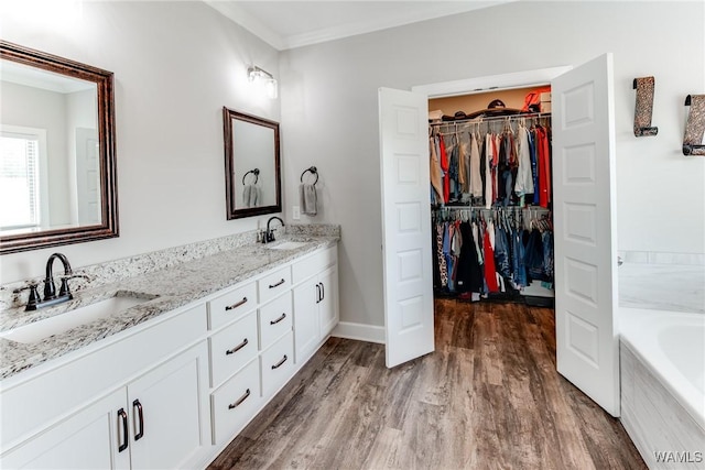 bathroom with ornamental molding, hardwood / wood-style floors, tiled bath, and vanity