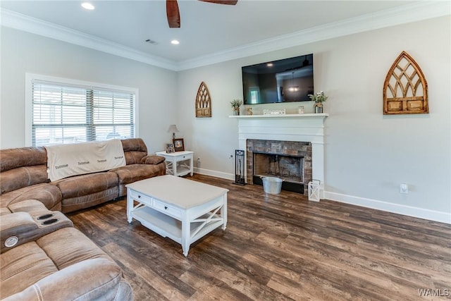 living room featuring dark wood-type flooring, ceiling fan, crown molding, and a stone fireplace