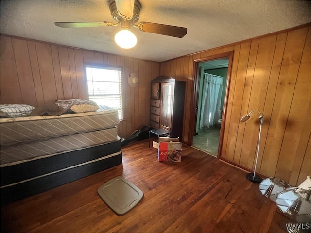 bedroom with dark wood-type flooring, wood walls, ceiling fan, and a textured ceiling