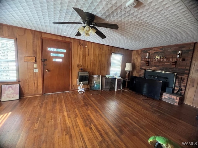 unfurnished living room featuring heating unit, hardwood / wood-style flooring, ceiling fan, and a wood stove