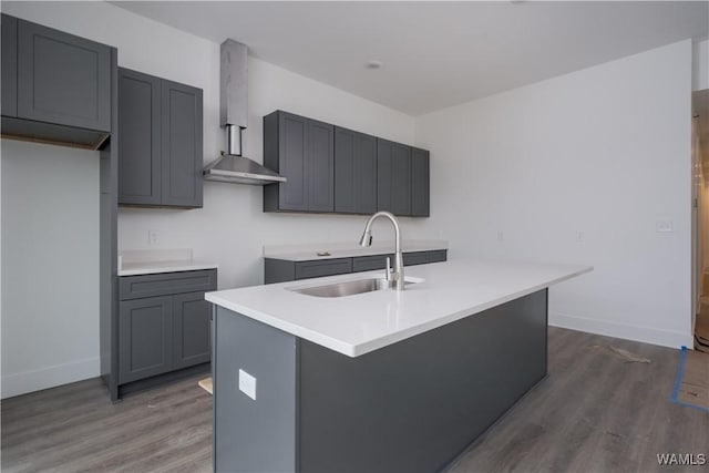 kitchen with sink, wall chimney range hood, gray cabinetry, and an island with sink