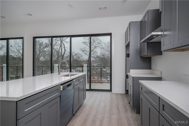 kitchen with light wood-type flooring, gray cabinetry, dishwashing machine, sink, and wall chimney range hood