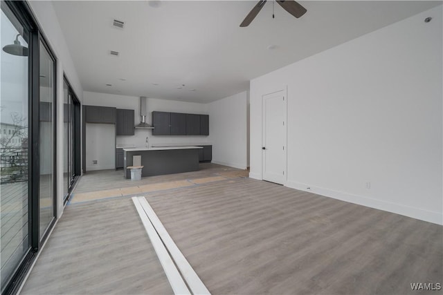 unfurnished living room with ceiling fan, sink, and light wood-type flooring