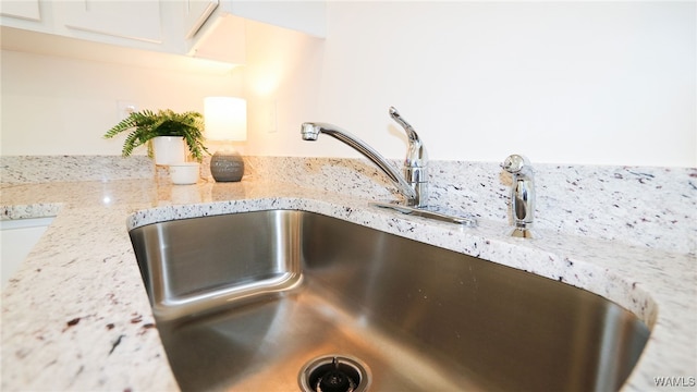 interior details with white cabinets, light stone countertops, and sink