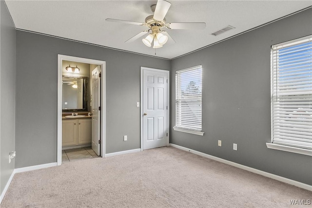 unfurnished bedroom featuring light carpet, sink, ensuite bath, and ceiling fan