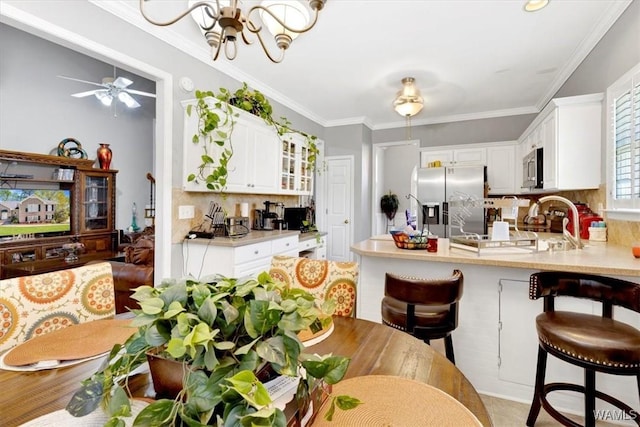 kitchen with backsplash, appliances with stainless steel finishes, a kitchen breakfast bar, ornamental molding, and white cabinets