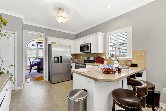 kitchen featuring white cabinets, appliances with stainless steel finishes, a kitchen bar, tasteful backsplash, and kitchen peninsula