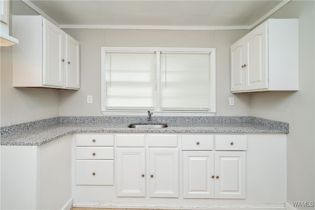 kitchen featuring white cabinets, light stone counters, and sink