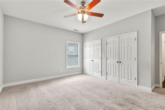 unfurnished bedroom with carpet, two closets, and ceiling fan