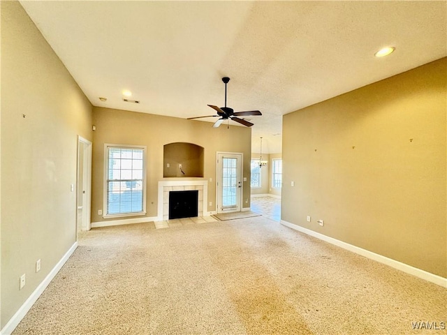 unfurnished living room with ceiling fan, a wealth of natural light, light colored carpet, and a tiled fireplace