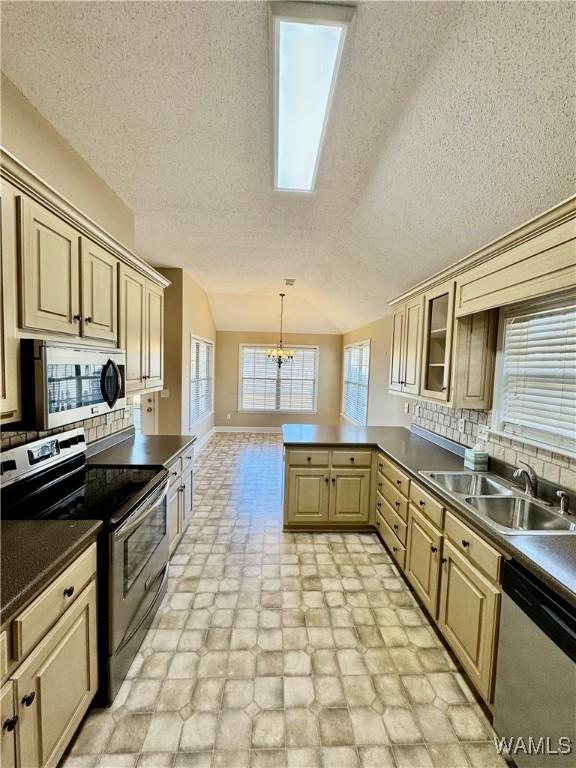 kitchen featuring lofted ceiling, stainless steel appliances, sink, backsplash, and a notable chandelier