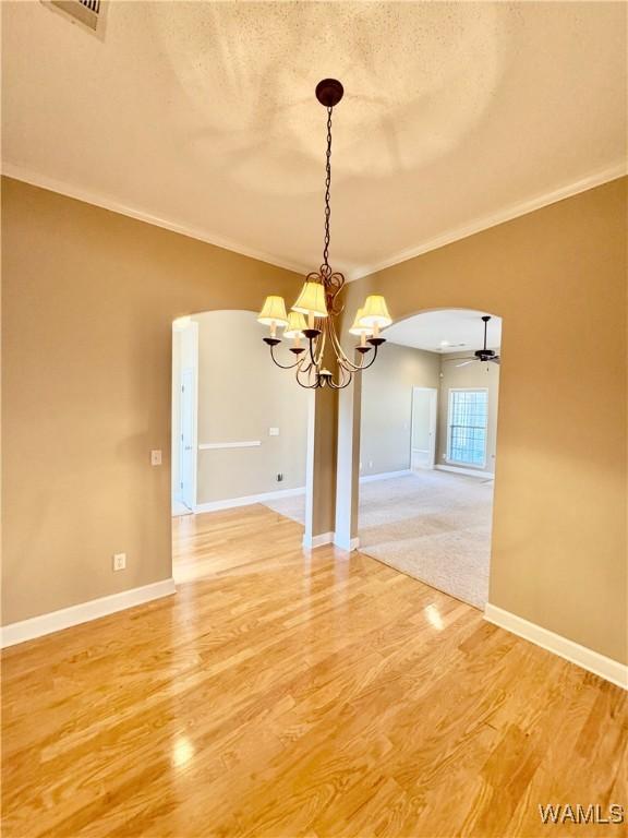 unfurnished dining area featuring crown molding, ceiling fan with notable chandelier, a textured ceiling, and hardwood / wood-style flooring