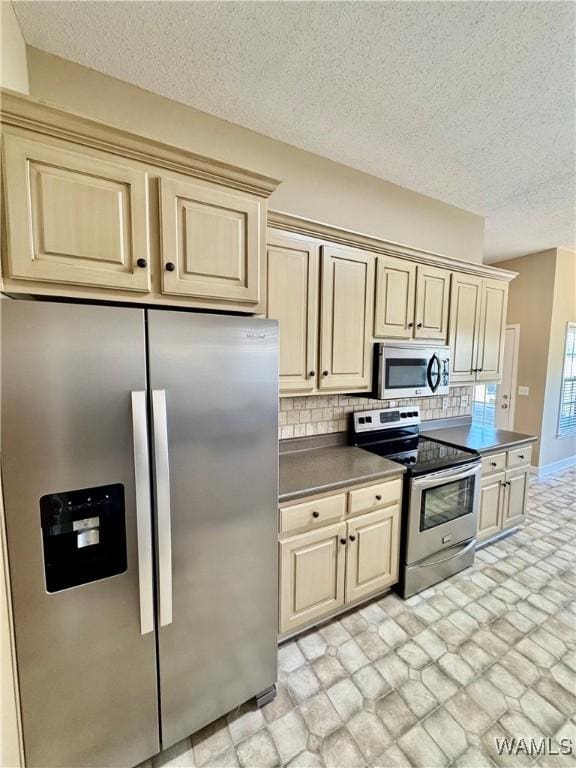 kitchen with decorative backsplash, a textured ceiling, stainless steel appliances, and cream cabinetry