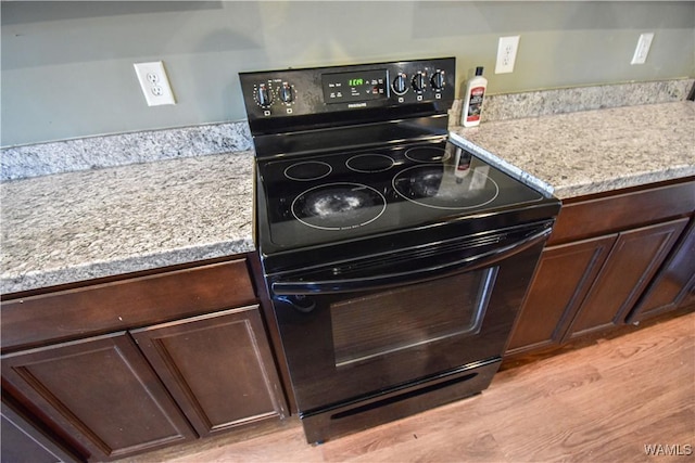 kitchen featuring dark brown cabinets, light wood-type flooring, black range with electric stovetop, and light stone counters