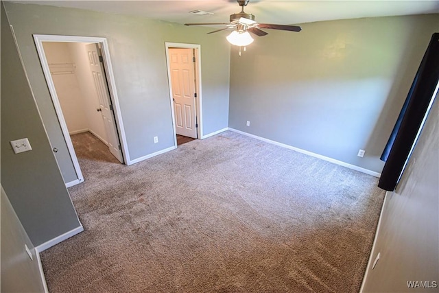 unfurnished bedroom featuring a walk in closet, ceiling fan, a closet, and dark colored carpet