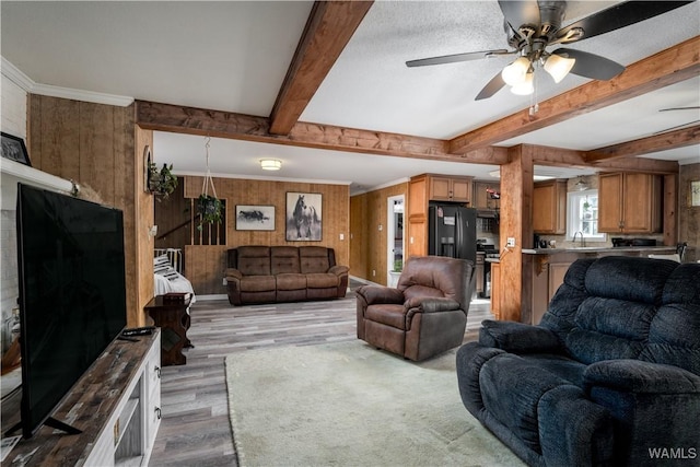 living room featuring ceiling fan, wooden walls, light hardwood / wood-style floors, and sink