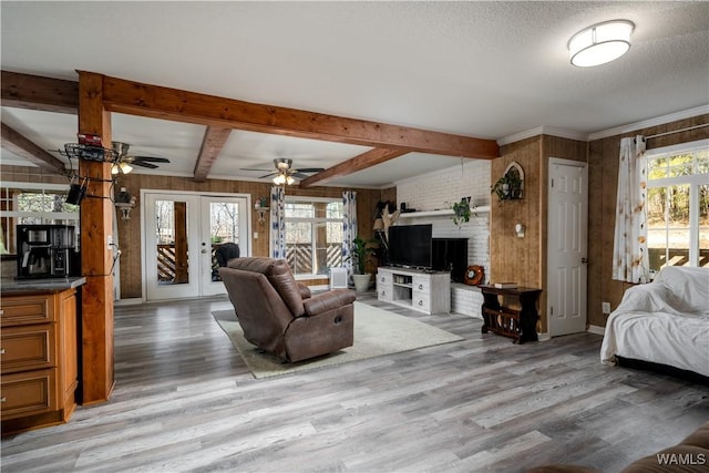 living room featuring ceiling fan, french doors, wooden walls, and beamed ceiling