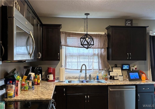 kitchen featuring a textured ceiling, a sink, light countertops, appliances with stainless steel finishes, and decorative light fixtures