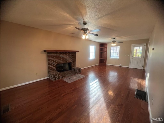 unfurnished living room featuring ceiling fan, dark wood-type flooring, a textured ceiling, and a brick fireplace