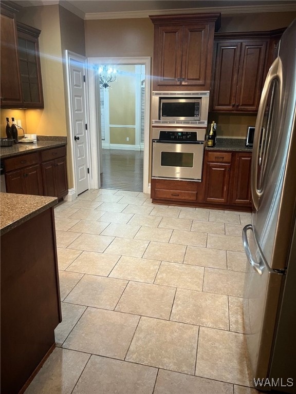 kitchen with dark stone counters, ornamental molding, dark brown cabinetry, stainless steel appliances, and an inviting chandelier