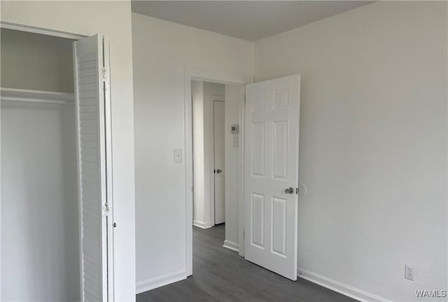 unfurnished bedroom with a closet, baseboards, and dark wood finished floors