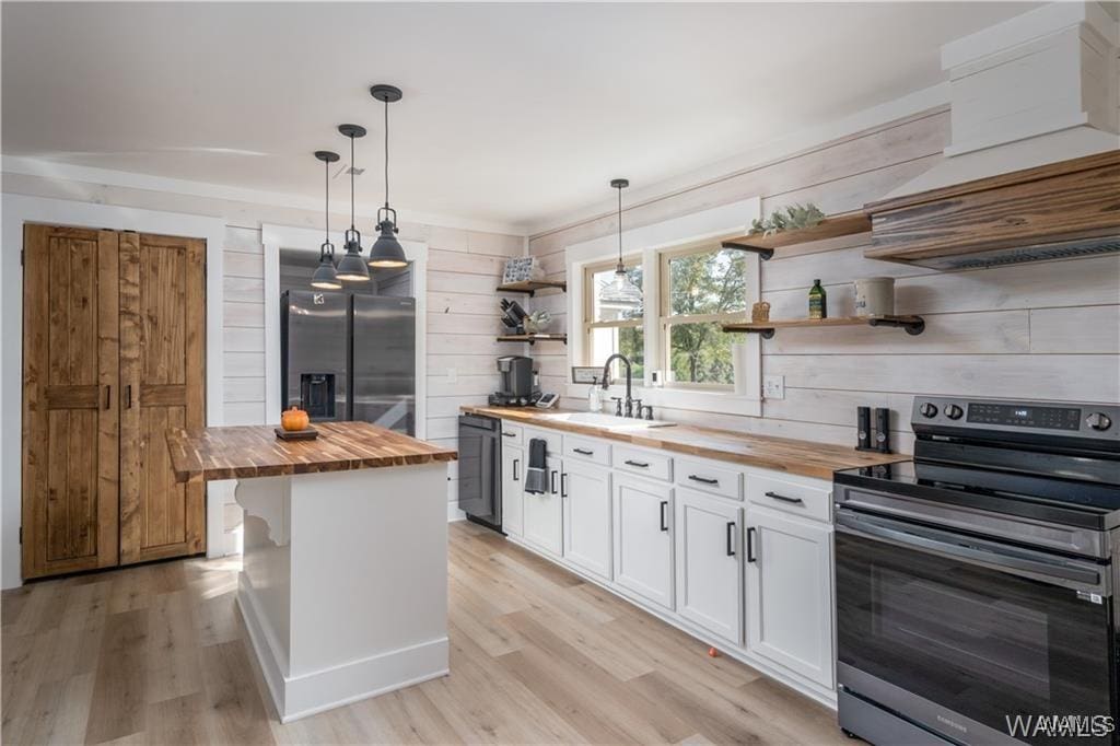 kitchen featuring pendant lighting, a center island, white cabinets, appliances with stainless steel finishes, and butcher block counters