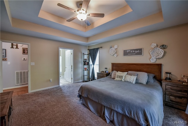 bedroom with carpet flooring, ceiling fan, connected bathroom, and a tray ceiling