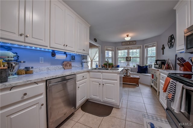 kitchen featuring kitchen peninsula, appliances with stainless steel finishes, light stone countertops, sink, and white cabinetry