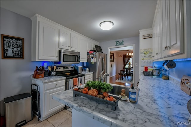 kitchen featuring light stone countertops, appliances with stainless steel finishes, light tile patterned floors, white cabinets, and a chandelier