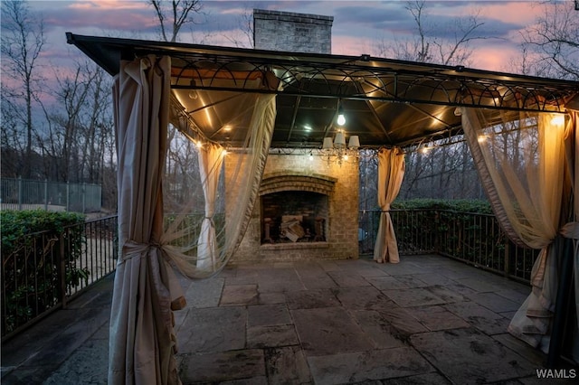 patio terrace at dusk with an outdoor brick fireplace and a gazebo