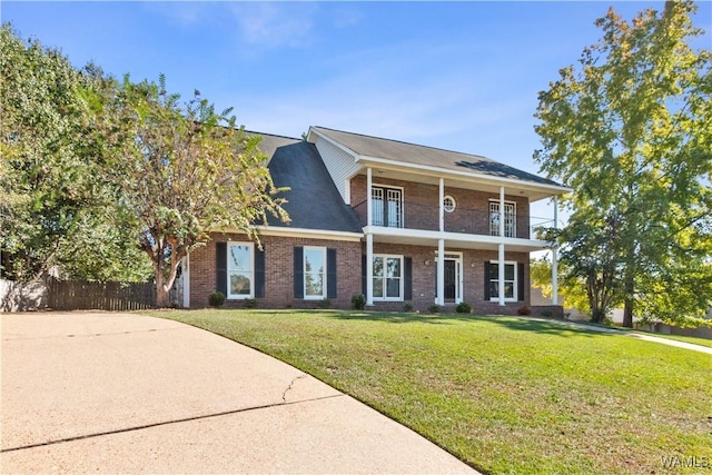 neoclassical / greek revival house with brick siding, a front lawn, a balcony, and fence