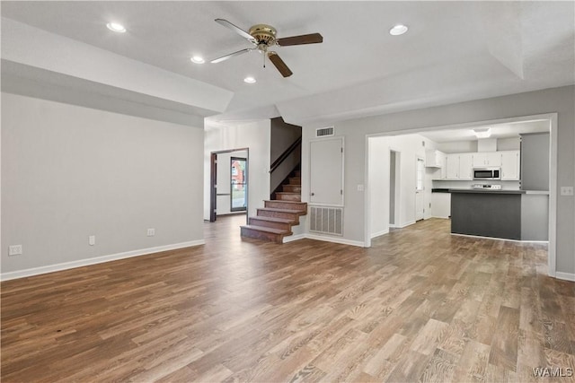 unfurnished living room with stairway, baseboards, visible vents, and wood finished floors