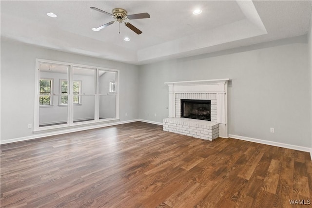 unfurnished living room with a brick fireplace, a raised ceiling, baseboards, and wood finished floors