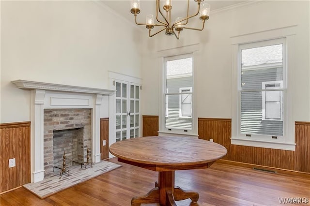 unfurnished dining area featuring an inviting chandelier, hardwood / wood-style flooring, wooden walls, a fireplace, and ornamental molding